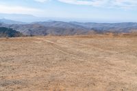 a dog is on a dirt hill while looking at the mountains from atop a mountain