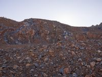 a large pile of rocks is sitting on top of a mountain side with the moon in the distance