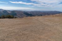 a car on dirt road at top of a mountain above hills with trees on a hill