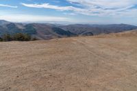 a car on dirt road at top of a mountain above hills with trees on a hill