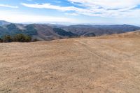 a car on dirt road at top of a mountain above hills with trees on a hill