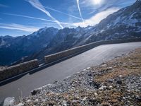 the man is riding on his bike down the road with mountains in the background and blue sky