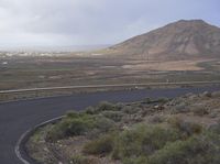 a curved road with no traffic on it that runs on the mountain side above a valley in the distance