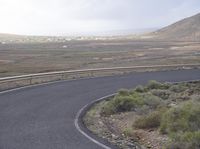 a curved road with no traffic on it that runs on the mountain side above a valley in the distance