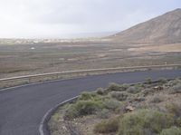 a curved road with no traffic on it that runs on the mountain side above a valley in the distance