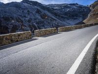 a road running between two mountains with a stone wall and fence in the center of it