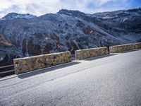 a road running between two mountains with a stone wall and fence in the center of it