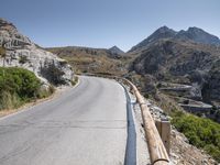 an asphalt mountain side near the road in the desert with steep hills around it and a mountain top to one side