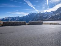 a paved mountain area with a road winding to the side with snow capped mountains in the background