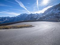 a paved mountain area with a road winding to the side with snow capped mountains in the background