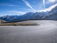 a paved mountain area with a road winding to the side with snow capped mountains in the background