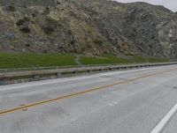 the side of the road on the side of a mountain with two yellow lines in front and one on the other