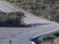 a small white car parked at the side of a winding mountain road near trees and bushes