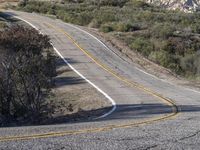 a small white car parked at the side of a winding mountain road near trees and bushes