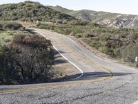 a small white car parked at the side of a winding mountain road near trees and bushes