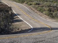 a small white car parked at the side of a winding mountain road near trees and bushes