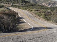 a small white car parked at the side of a winding mountain road near trees and bushes