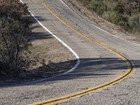 a small white car parked at the side of a winding mountain road near trees and bushes