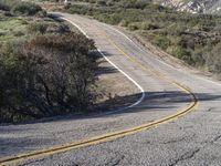 a small white car parked at the side of a winding mountain road near trees and bushes