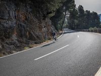 a black motorcycle rides past the edge of a rocky cliff formation at dusk on a highway