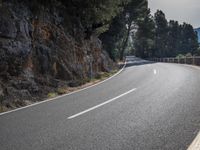 a black motorcycle rides past the edge of a rocky cliff formation at dusk on a highway