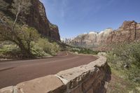 a curved road with red rocks and trees on both sides in front of some cliffs