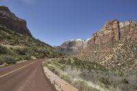 a curved road with red rocks and trees on both sides in front of some cliffs
