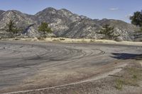 a view along a dirt road of an empty field and mountains in the distance of the scene