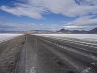 a lone, empty road leads through the desert landscape of the horizon line, with snow in the foreground