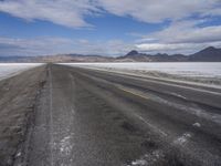 a lone, empty road leads through the desert landscape of the horizon line, with snow in the foreground