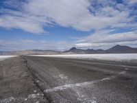 a lone, empty road leads through the desert landscape of the horizon line, with snow in the foreground