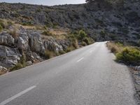 a lone motorcycle is riding in the road beside a rock cliff wall and scrubby