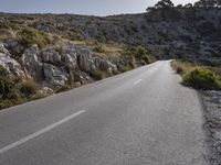 a lone motorcycle is riding in the road beside a rock cliff wall and scrubby