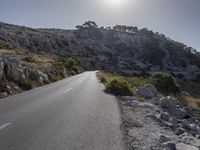 a lone motorcycle is riding in the road beside a rock cliff wall and scrubby