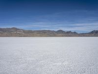 snow on the desert with mountains in the background and a single bench sitting on top of a bench