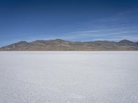 snow on the desert with mountains in the background and a single bench sitting on top of a bench