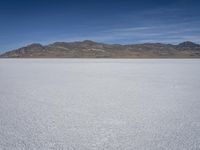 snow on the desert with mountains in the background and a single bench sitting on top of a bench