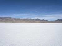 snow on the desert with mountains in the background and a single bench sitting on top of a bench