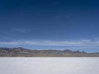 snow on the desert with mountains in the background and a single bench sitting on top of a bench