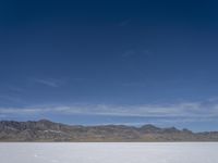 snow on the desert with mountains in the background and a single bench sitting on top of a bench