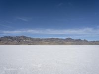 snow on the desert with mountains in the background and a single bench sitting on top of a bench