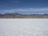 snow on the desert with mountains in the background and a single bench sitting on top of a bench