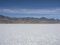 snow on the desert with mountains in the background and a single bench sitting on top of a bench