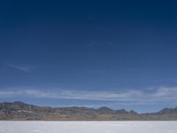 snow on the desert with mountains in the background and a single bench sitting on top of a bench