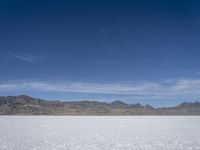 snow on the desert with mountains in the background and a single bench sitting on top of a bench