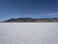 snow on the desert with mountains in the background and a single bench sitting on top of a bench