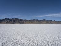 snow on the desert with mountains in the background and a single bench sitting on top of a bench