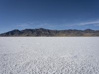 snow on the desert with mountains in the background and a single bench sitting on top of a bench