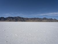 snow on the desert with mountains in the background and a single bench sitting on top of a bench