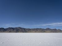 snow on the desert with mountains in the background and a single bench sitting on top of a bench